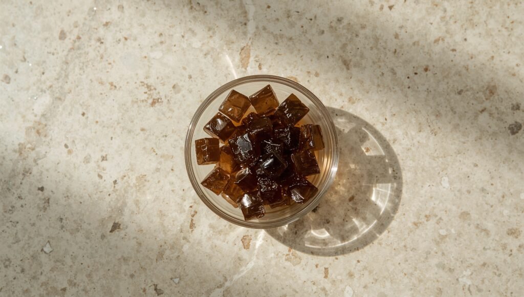 Clear glass bowl of dark translucent grass jelly cubes on light terrazzo.