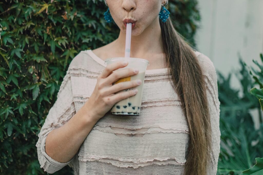 CoCo Fresh Bubble Tea calories—person sipping milk tea through a wide straw, holding a clear cup with pearls, logo not visible, outdoor greenery background