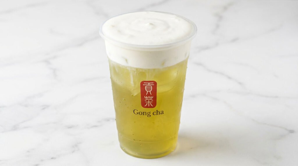 Gong Cha Milk Foam Green Tea in a clear cup with a thick layer of white cream mousse on a marble table.